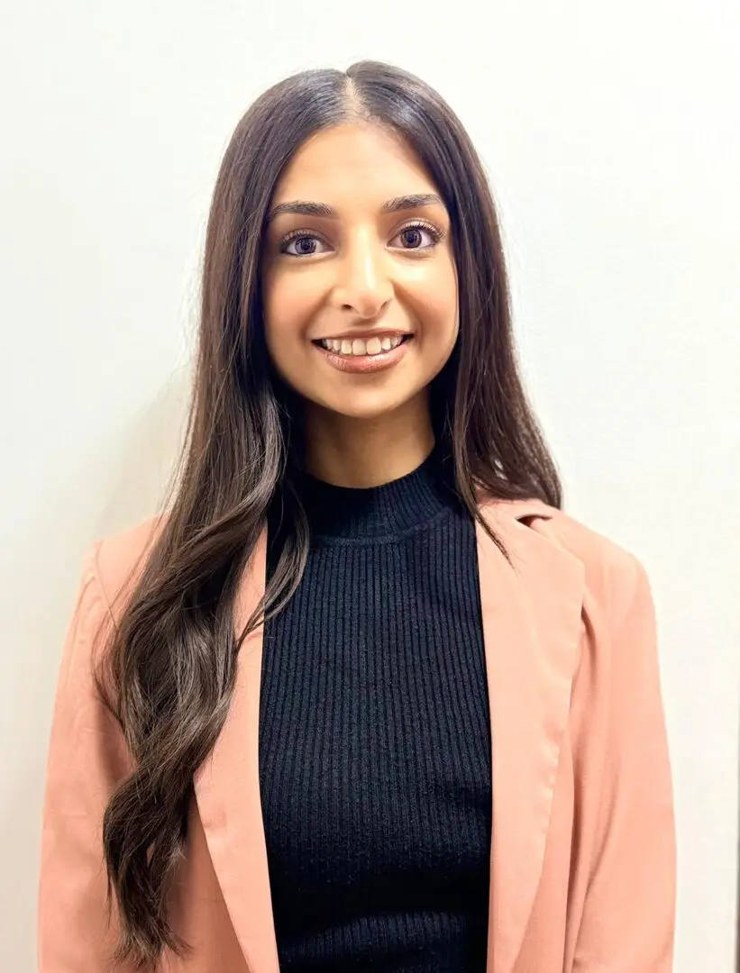 Portrait of a smiling young woman with long dark hair in a peach blazer.